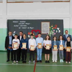 Nauczycielka wyczytuje uczniów nagrodzonych w ogólnopolskim konkursie literackim, w tyle ksiądz.