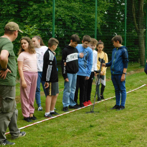 uczniowie podczas zabawy „pole minowe”. Jeden z uczniów próbuje odszukać ukryte w ziemi przedmioty za pomocą wykrywania metalu.