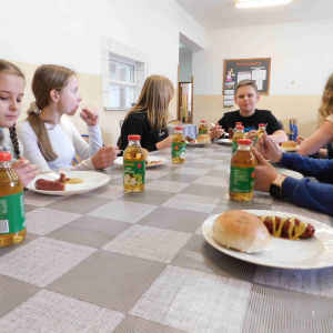 Uczniowie klasy siódmej na stołówce szkolnej konsumują kiełbaski.