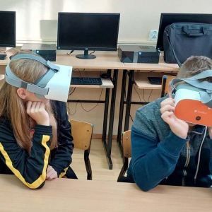 Uczniowie w okularach VR na tle laptopów.