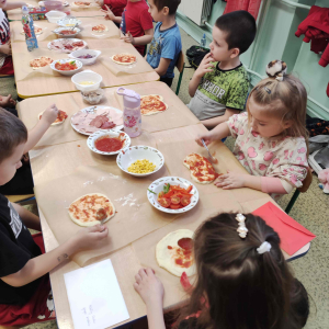 Przedszkolaki nakładają sos na pizzę