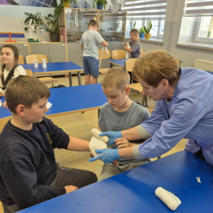 Pani Kazimiera Ligaj pokazuje, jak prawidłowo założyć opatrunek na rękę.
