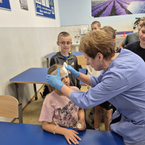 Demonstracja prawidłowego bandażowania głowy – uczniowie z uwagą obserwują pokaz.