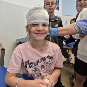 Uczennica, z uśmiechem i dumą z nowej umiejętności. prezentuje efekt ćwiczeń z bandażowania.