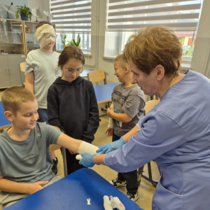 Pani Kazimiera Ligaj pomaga uczniowi w prawidłowym zabandażowaniu ręki – nauka przez praktykę.
