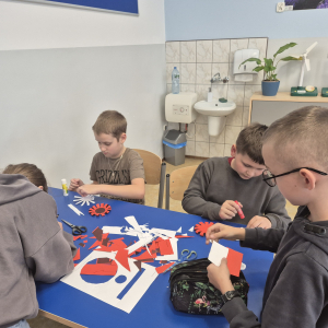 Praca nad elementami kokard narodowych.  Sklejanie kolejnych części biało-czerwonych kotylionów.