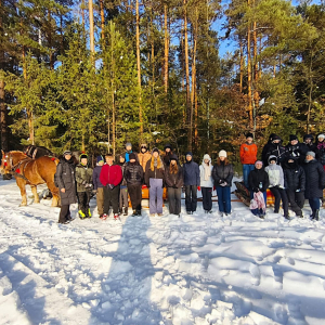 Grupa uczniów klas 6 i 8 wraz z opiekunami w zimowej scenerii na tle sań i koni